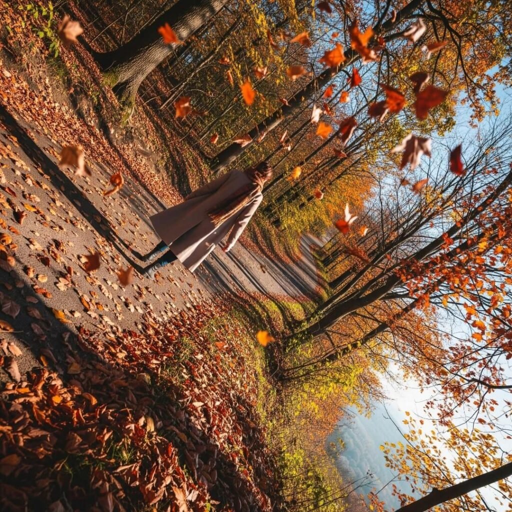 A photograph of a woman walking a winding path with autumn leaves falling around her.